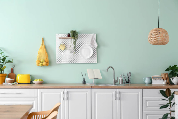 Wnętrze stylowej kuchni z białymi licznikami i deską wiszącą na zielonej ścianie - Zdjęcie, obraz