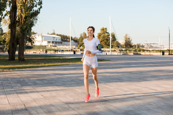Όμορφη νεαρή γυναίκα με ακουστικά τρέχει στο πάρκο - Φωτογραφία, εικόνα