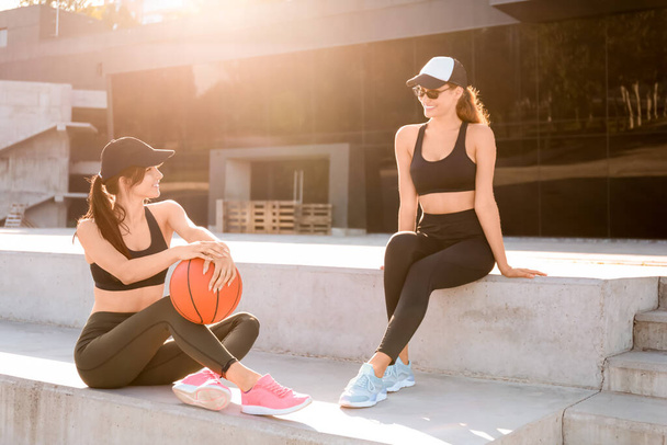 Sporty young women with ball sitting on stairs outdoors - Foto, imagen