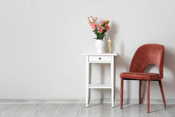 Moderner Stuhl und Tisch mit Vase, Rosen und Schaufensterpuppe an heller Wand - Foto, Bild