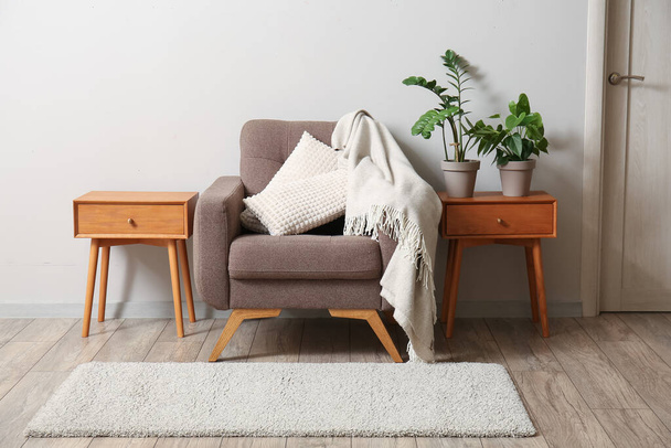 Soft armchair and wooden tables with houseplants near light wall - Φωτογραφία, εικόνα