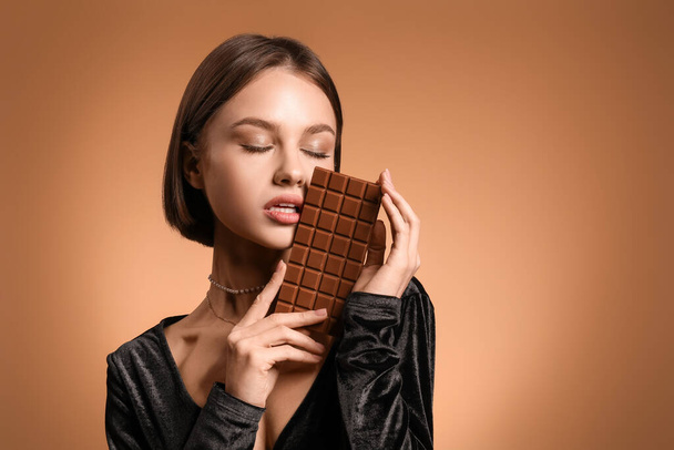 Mooie vrouw met zoete chocolade op kleur achtergrond - Foto, afbeelding