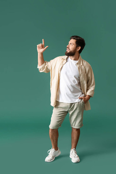 Handsome man in white t-shirt pointing at something on green background - Photo, image