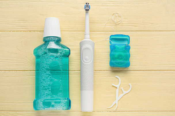 Zahnseide mit Zahnstocher, elektrischer Bürste und Spülung auf gelbem Holzhintergrund - Foto, Bild