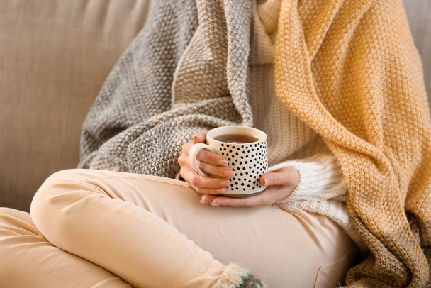 Νεαρή γυναίκα πίνει νόστιμο τσάι στον καναπέ στο σπίτι, κοντινό πλάνο - Φωτογραφία, εικόνα
