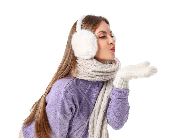 Beautiful young woman in warm winter clothes sending air kiss on white background - Foto, Bild