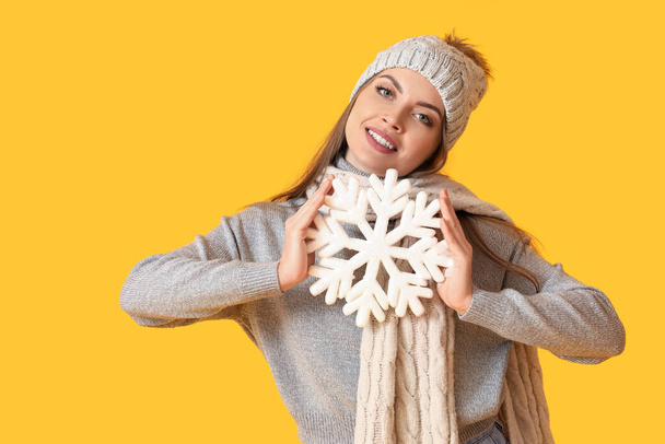 Beautiful young woman in warm winter clothes and with snowflake on color background - Foto, afbeelding