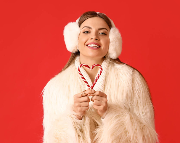 Krásná mladá žena v teplém zimním oblečení a s cukrovou třtinou na barevném pozadí - Fotografie, Obrázek