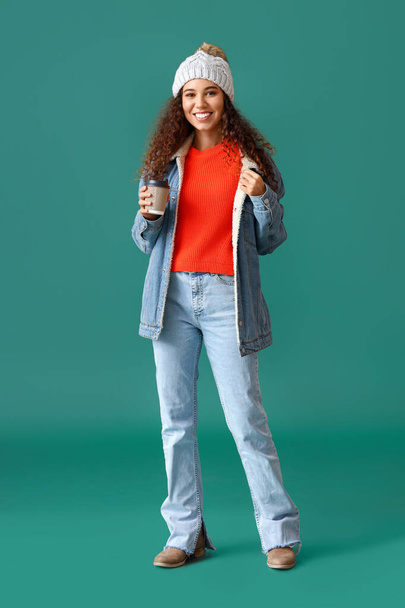 Hermosa mujer joven en ropa de invierno con estilo y con taza de café en el fondo de color - Foto, Imagen