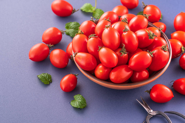 Fresh cherry tomatoes in a wooden bowl isolated on a blue background, close up, copy space - Foto, imagen