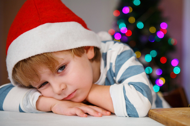 kleiner Junge mit Weihnachtsmütze mit Weihnachtsbaum und Lichtern - Foto, Bild