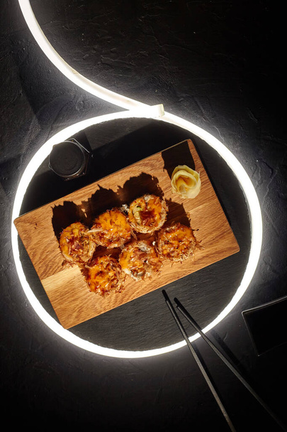 Fried sushi rolls with melted cheese and bonito flakes on black background with LED strip - Foto, Bild