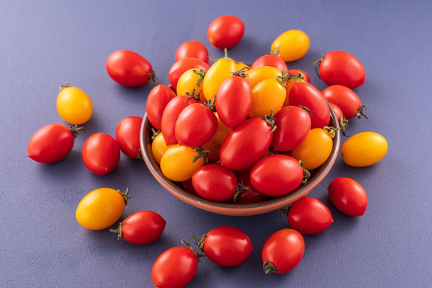 Fresh cherry tomatoes in a wooden bowl isolated on a blue background, close up, copy space - Фото, зображення