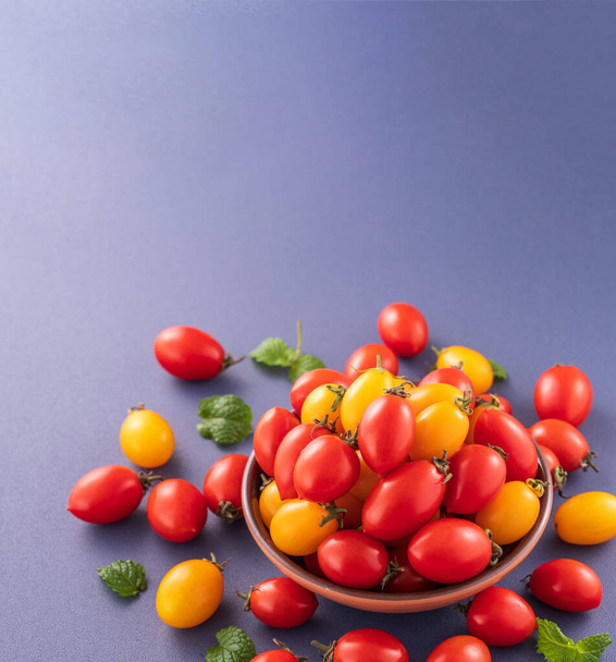 Fresh cherry tomatoes in a wooden bowl isolated on a blue background, close up, copy space - Zdjęcie, obraz