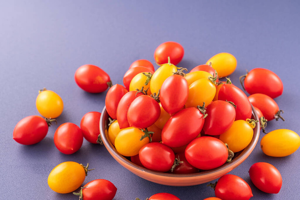 Fresh cherry tomatoes in a wooden bowl isolated on a blue background, close up, copy space - Fotografie, Obrázek