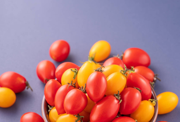 Fresh cherry tomatoes in a wooden bowl isolated on a blue background, close up, copy space - 写真・画像