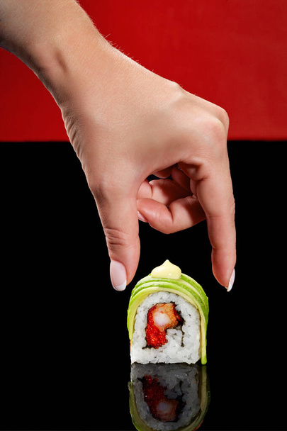Mão feminina tomando rolo de sushi com camarão, ovas de peixe voador, abacate e maionese japonesa - Foto, Imagem