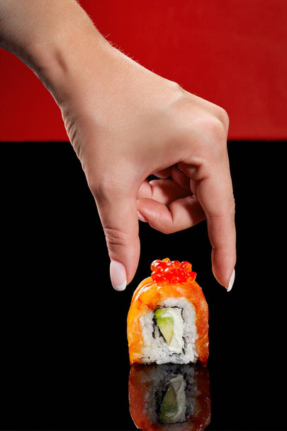 Female hand reaching out to Philadelphia sushi roll with salmon, cream cheese, avocado and red caviar - Foto, Bild
