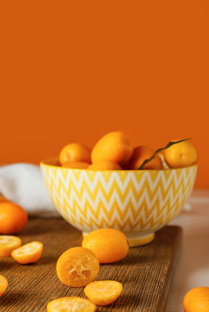 Cuenco con sabrosas frutas kumquat en la mesa contra la pared naranja - Foto, imagen