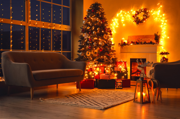Stijlvol interieur van woonkamer met mooie kerstboom en open haard 's nachts - Foto, afbeelding