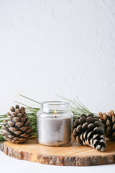 Tablero con conos de pino, vela encendida y rama de abeto sobre fondo claro - Foto, Imagen