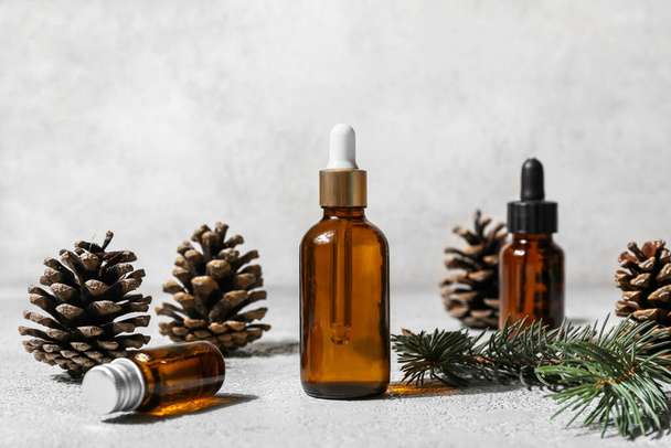 Bottles of essential oil, fir branch and pine cones on light background - Fotó, kép