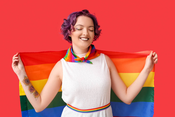 Mujer joven con bandera LGBT sobre fondo rojo - Foto, Imagen
