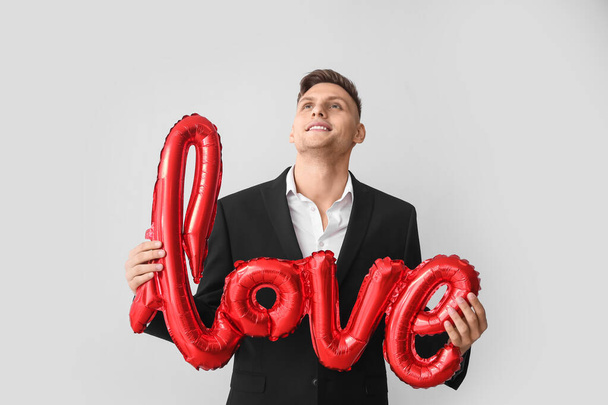 Mladý muž s balónem ve tvaru slova LOVE na šedém pozadí. Valentýnská oslava - Fotografie, Obrázek