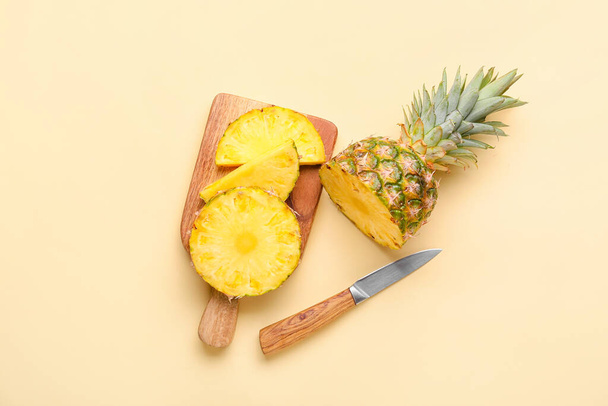 Деревянная доска с разрезанным ананасом и ножом на цветном фоне - Фото, изображение