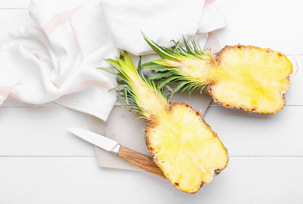 Bord met vers gesneden ananas en mes op een lichte houten ondergrond - Foto, afbeelding