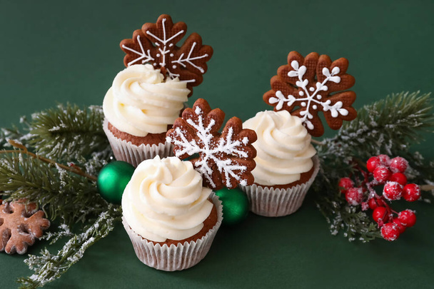 Tasty Christmas cupcakes with gingerbread cookies and decor on green background - Foto, Bild