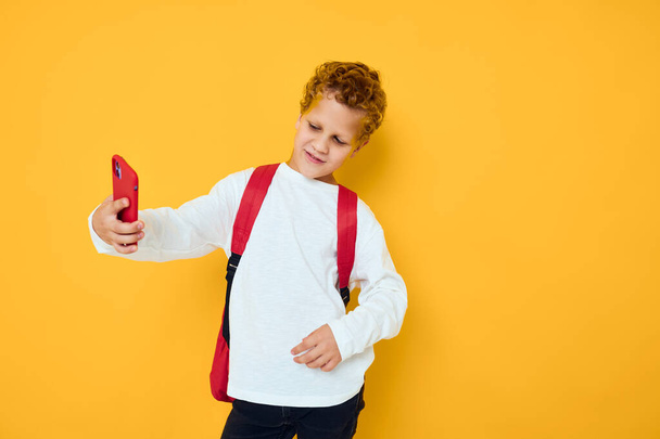 tinédzser fiú beszél telefonon egy iskolai hátizsák sárga háttér - Fotó, kép