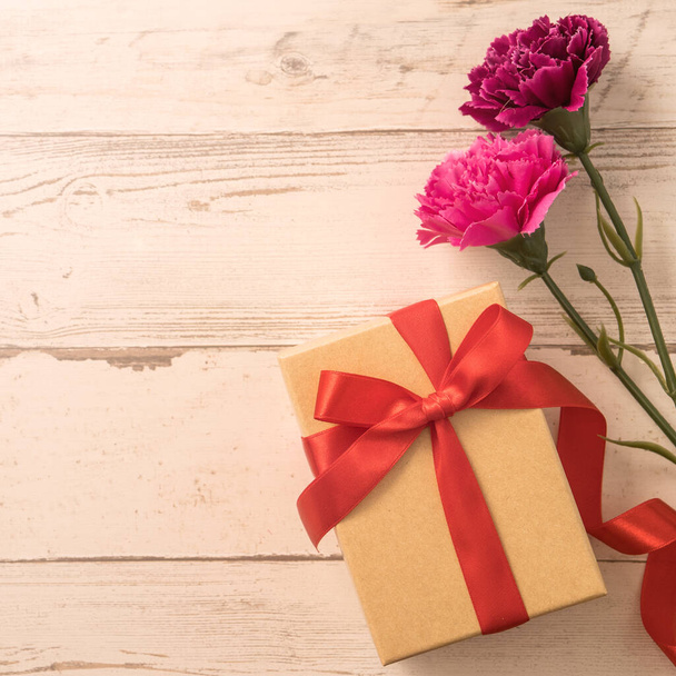 Kraft gift box with red ribbon bow and carnation, concept of giving present at mother's day as surprise, flat lay, top view - Fotoğraf, Görsel