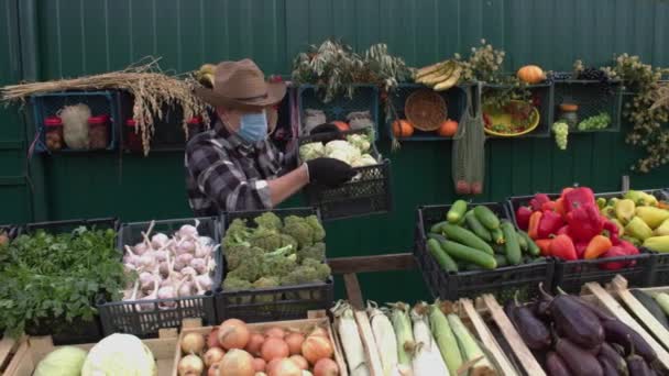 Cauliflower at the farmers' market. Slow Motion 2x.A male salesman places a box of cauliflower on the counter and then looks into the camera. The seller in a protective medical mask. - Footage, Video