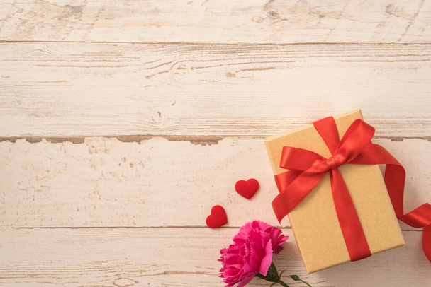 Kraftpapier geschenkdoos met rood lint strik en anjer, concept om cadeau te geven op moederdag als verrassing, platte lay, bovenaanzicht - Foto, afbeelding