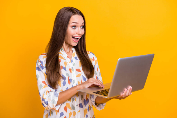 Photo portrait of excited girl browsing internet holding laptop isolated on vivid yellow colored background - Foto, Bild