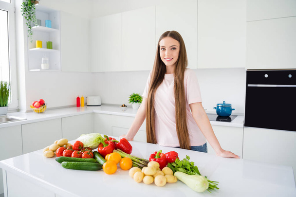 Portrait of attractive cheerful long-haired girl preparing useful food vegan green salad at home light white kitchen indoors - Fotó, kép
