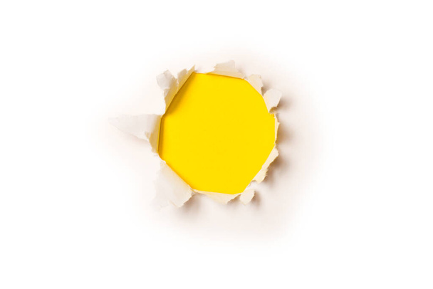 Ein Loch in einem weißen Papier auf gelbem Hintergrund, Kopierraum.  - Foto, Bild