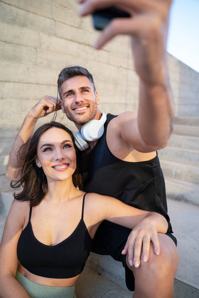 Attractive happy couple taking a selfie with a smartphone after outdoor workout. Sport and healthy lifestyle concept. Personal Trainer. Morning routine.  - Foto, imagen