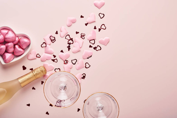 Valentines day greeting card with champagne bottle, tow glasses, chocolate hearts and gift box on pink background. Top view with space for greetings. Greeting card with copy space. - Fotó, kép