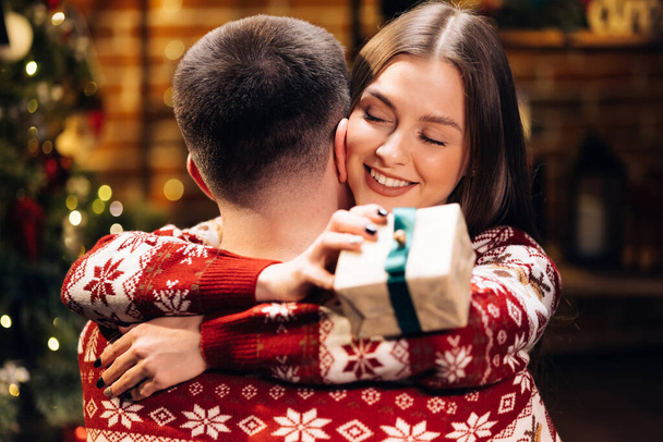 Close up of caucasian family embracing standing near decorated glowing fir tree. Happy wife feels grateful hugs husband express gratitude for New Year gift. Christmas holidays celebration concept - Valokuva, kuva