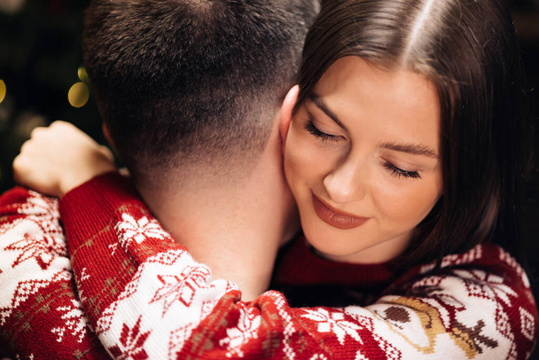 Close up of young beautiful woman hugging man holding Christmas present. Family tradition. Exchange of gifts. Christmas holidays celebration concept. - 写真・画像