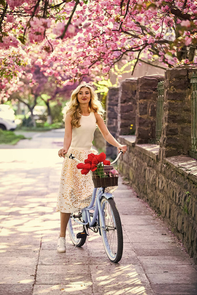 Spring style travel. retro woman sell tulip flower bouquet. girl under sakura with vintage bicycle. spring beauty and fashion. cherry tree pink blossom. perfect smell. perfume spa and allergic - Foto, imagen