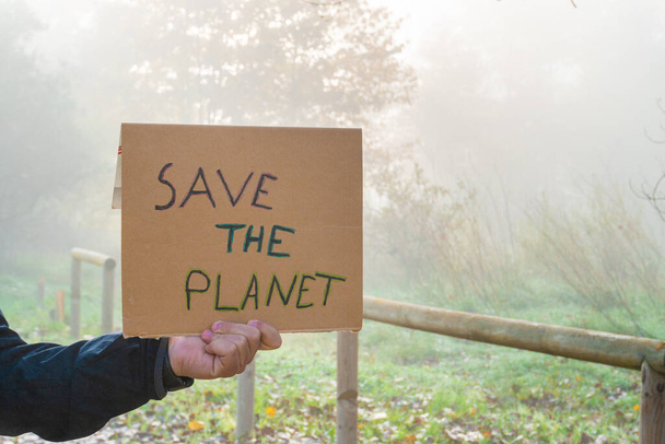 The Male hands hold a cardboard sign with the slogan Save the Planet with the forest in background - Φωτογραφία, εικόνα