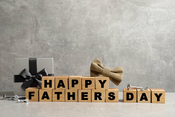 Cubes with phrase Happy Father's Day, bow tie and gift box on grey background. Space for text - Foto, Imagem