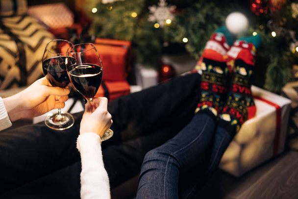 Adults people pouring wine into glasses for christmas and new year celebrations. Happy couple clink wine glasses toast and celebrate together New 2022 Year at home near glowing Christmas tree. - Foto, immagini