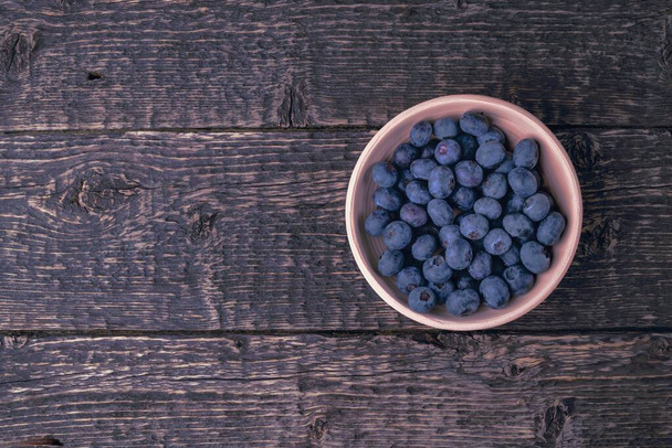 Clay bowl with blueberries on the texture of an old wood. Close-up, flat lay - Foto, Bild