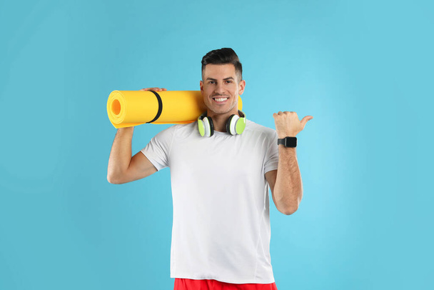 Handsome man with yoga mat and headphones on turquoise background - Fotografie, Obrázek