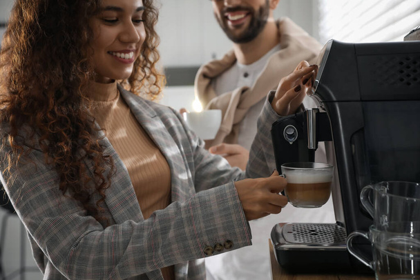 アフリカ系アメリカ人女性のオフィスで現代的なマシンと新鮮な香りのコーヒーを準備 - 写真・画像