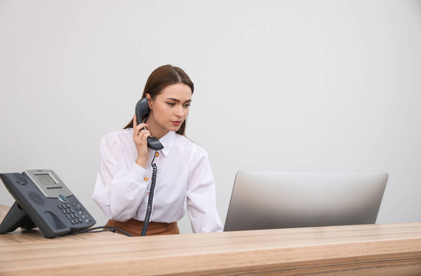 Female receptionist talking on phone at workplace - Фото, изображение